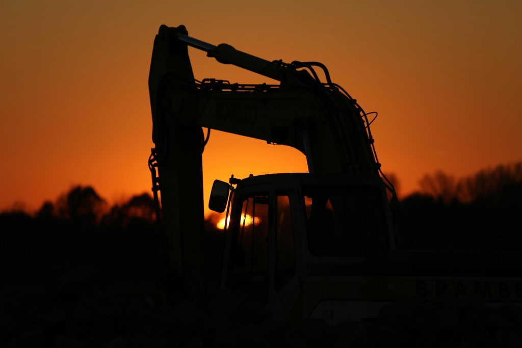 An excavator's silhouette set against a vibrant orange sunset sky